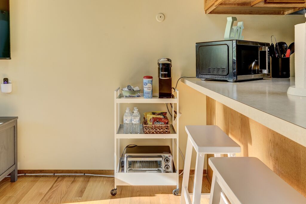 A compact kitchenette with a microwave, toaster, and a small shelf with bottled water and snacks.