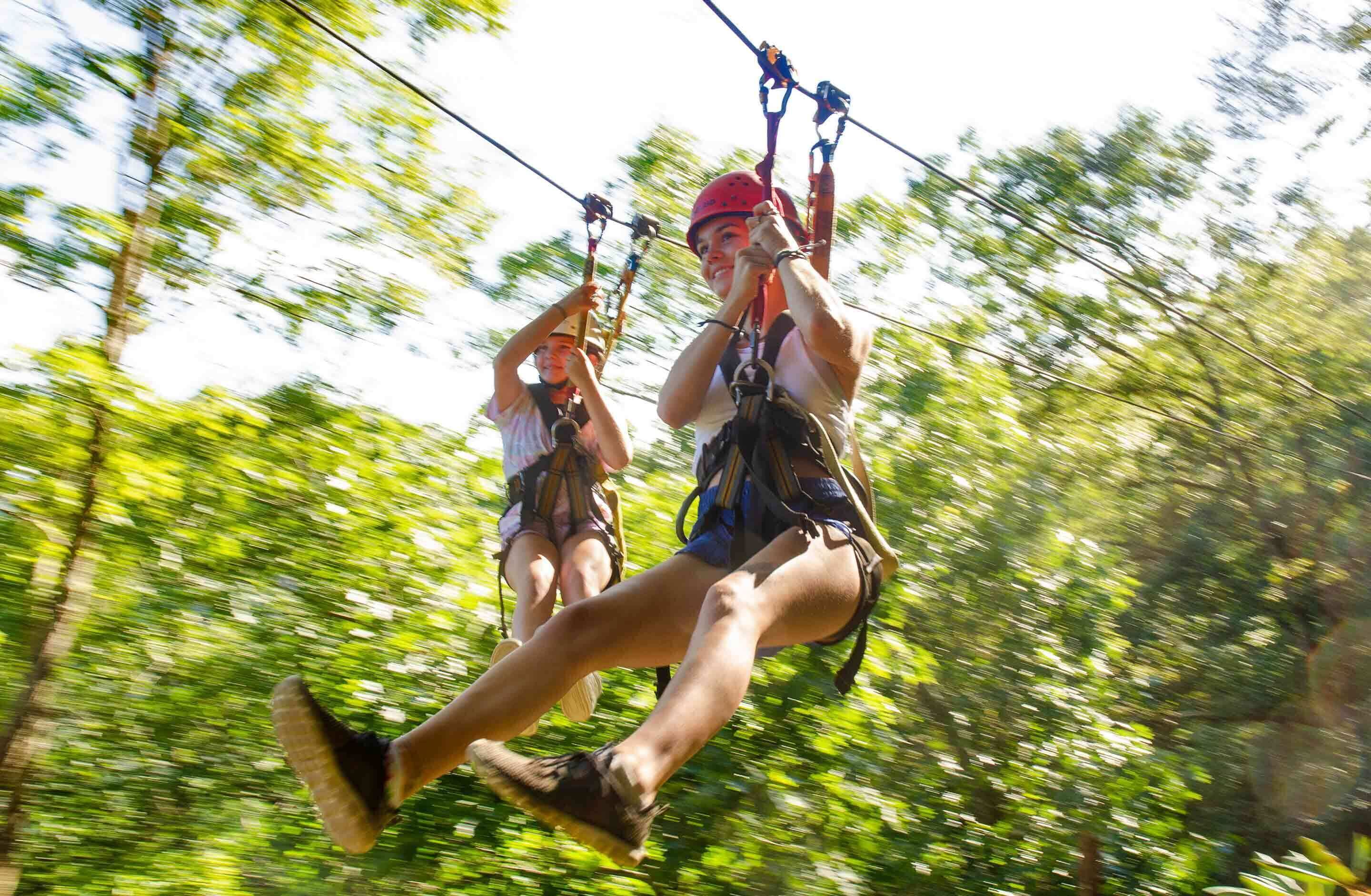 Two people zip-lining through a forested area.