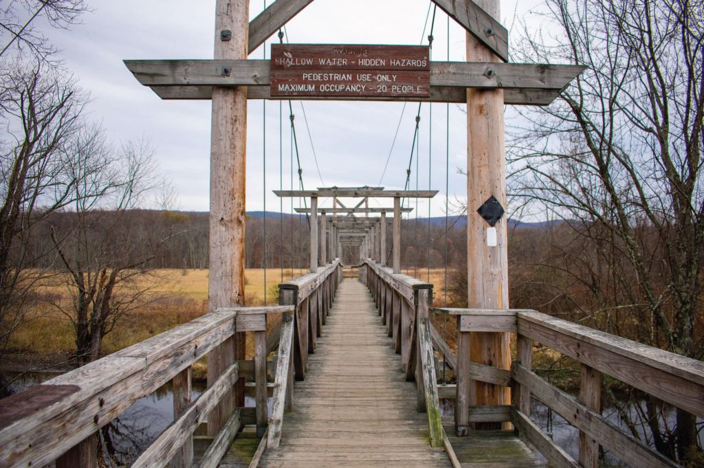 Un ponte pedonale in legno con un cartello che avverte di acque basse e pericoli nascosti.