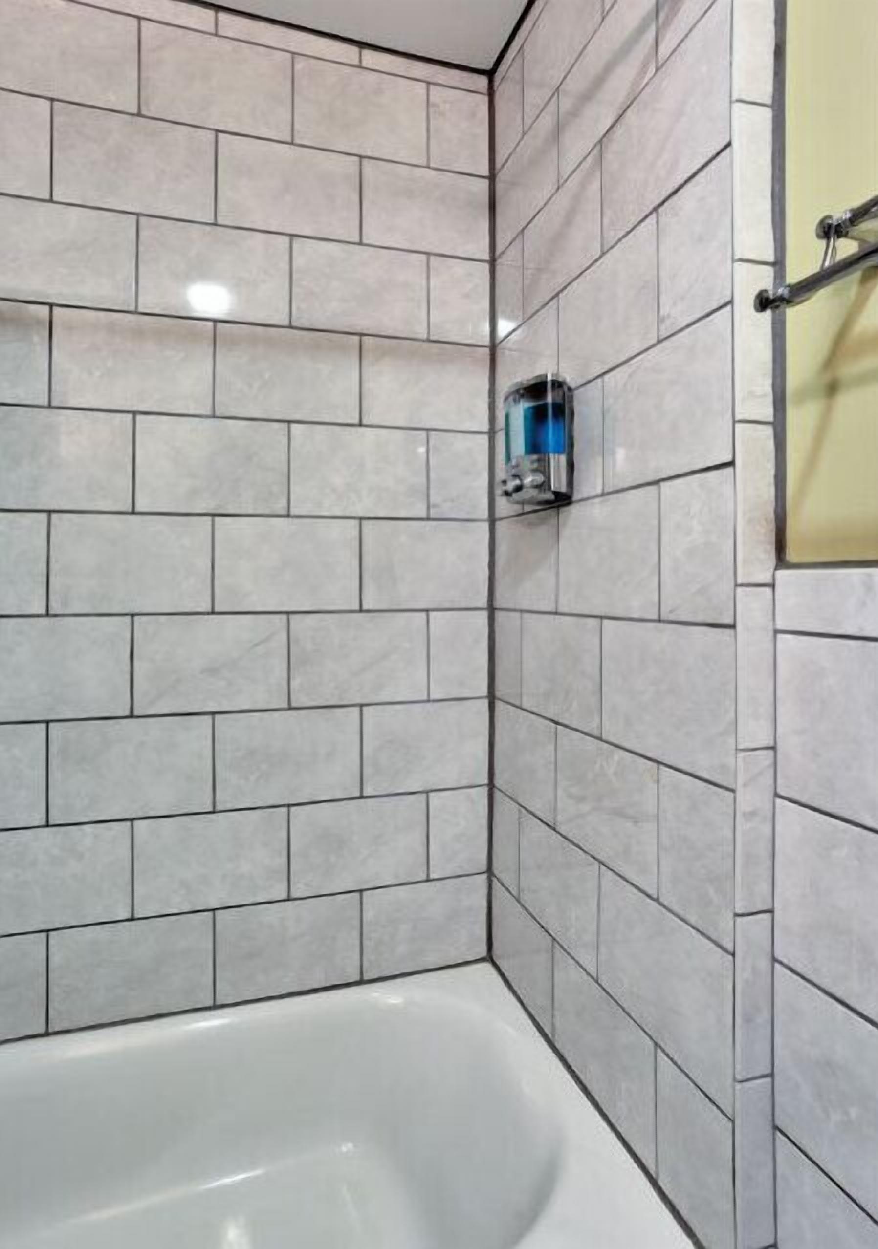 A bathroom with a white bathtub, grey tiled walls, and a glass shower enclosure.
