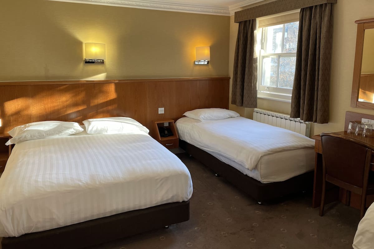 A hotel room with two beds, a desk, and a window with curtains.