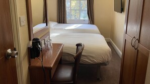 Une chambre d’hôtel avec deux lits, un bureau avec une chaise, un miroir et une fenêtre avec des rideaux.