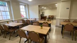 Un vaste espace dédié à la salle à manger, avec de nombreuses tables et chaises, des spots encastrés au plafond et de grandes fenêtres laissant entrer la lumière naturelle.