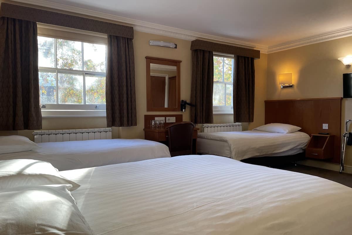 A hotel room with two beds, a desk, a chair, a mirror, and a window with curtains.