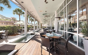 An outdoor dining area with tables and chairs, a pool, and large windows.