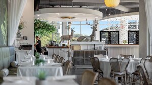 En restaurant med runde borde, et barområde og en stor hjortesulptur.