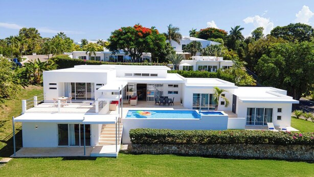 Ein modernes, mehrgeschossiges Haus mit Pool, überdachter Terrasse und üppiger Bepflanzung.