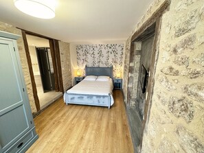 A bedroom with a bed, two bedside tables with lamps, a stone wall, and a wooden floor.