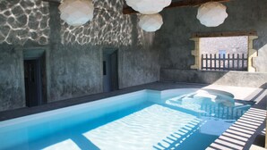 A swimming pool with a clear blue water surface, surrounded by stone walls and wooden beams.