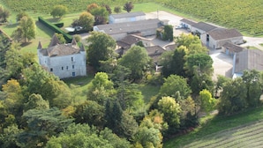 An aerial view of a historic estate with a large stone building, several smaller structures, and surrounding green fields.