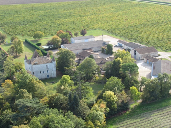 An aerial view of a historic estate with a large stone building, several smaller structures, and surrounding green fields.