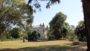 A stone building with a tiled roof, surrounded by trees and a grassy area.