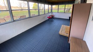 Ein überdachter Patio-Bereich mit blauem Boden, großen Fenstern und einem Tisch mit Stühlen.