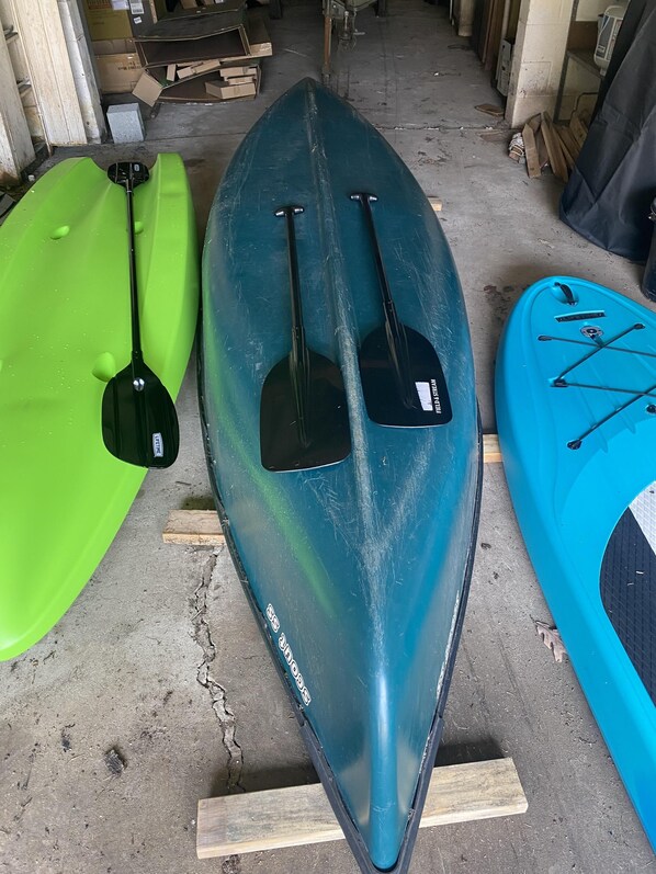 A row of kayaks and paddles in a storage area.