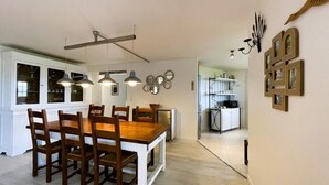 A dining area with a wooden table and chairs, pendant lights, and a kitchen in the background. - Le Belvue, a relaxing stay with a view of the Pyrenees mountain range  (ESTIALESCQ)
