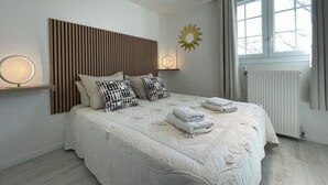 A modern bedroom with a large bed, a wooden headboard, a sun-shaped wall decoration, and a window with curtains. - Le Belvue, a relaxing stay with a view of the Pyrenees mountain range  (ESTIALESCQ)