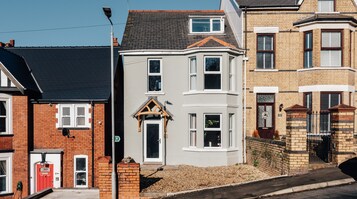 A two-story house with a white facade, a dark roof, and a small front garden.