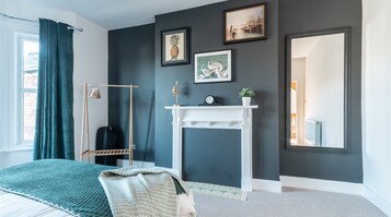 A bedroom with a bed, a hanging chair, a fireplace, and wall-mounted artwork.