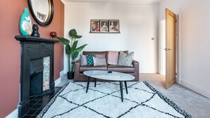 Una sala de estar con chimenea, un sofá de cuero marrón, una mesa de centro blanca y una planta grande.
