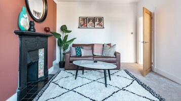 A living room with a fireplace, a brown leather sofa, a white coffee table, and a large plant.