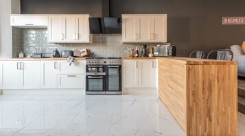 Una cocina moderna con armarios blancos, encimera de madera, horno empotrado y estufa negra.