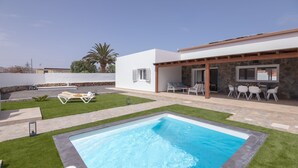 Un espace piscine extérieur moderne, doté d’un patio en pierre, d’un coin salon couvert et d’une pelouse bien entretenue.