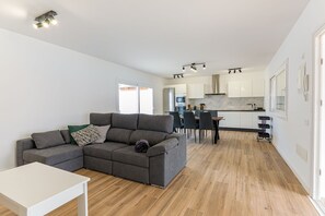 Ein modernes Wohnzimmer mit einem grauen Ecksofa, einem kleinen weißen Tisch und Holzböden.