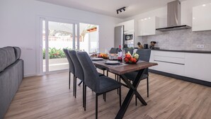 Une cuisine moderne avec des meubles blancs, une table à manger avec des chaises et une vue sur l’extérieur.