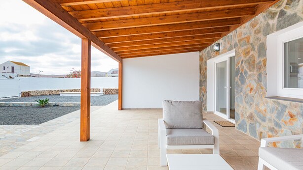 Une terrasse couverte avec des murs en pierre, un canapé blanc et une vue sur la mer.