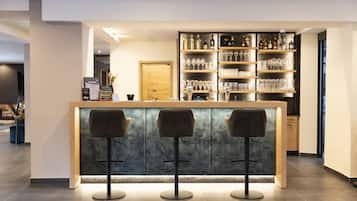 Eine Bar mit Marmorplatte, drei Barhocker und Regalen voller Gläser und Flaschen.