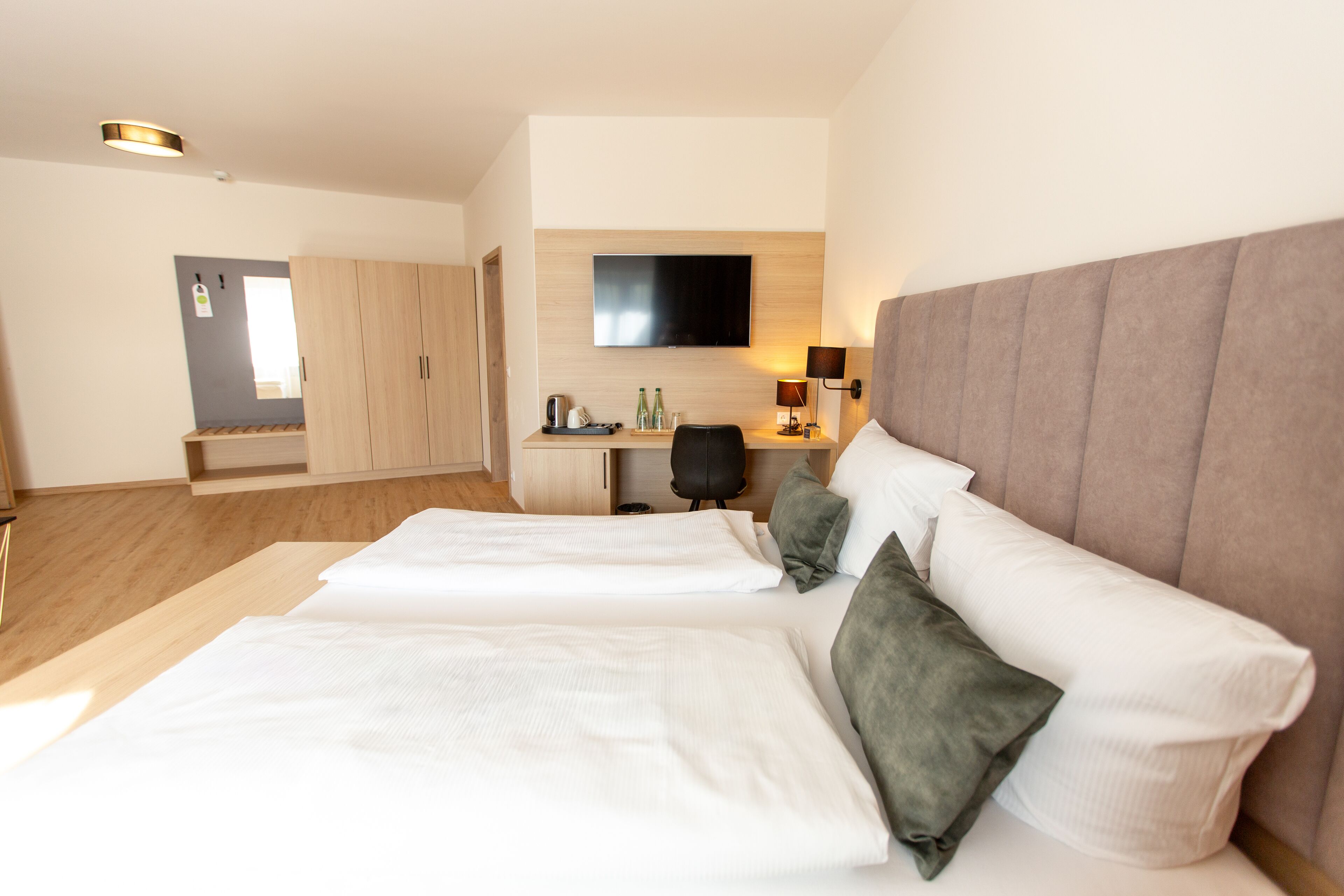 A hotel room with two beds, a desk, a flat-screen TV, and a wardrobe.