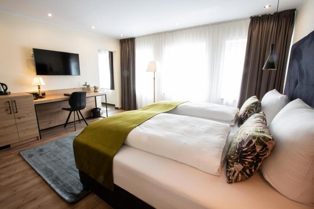 A hotel room with a bed, desk, chair, TV, and curtains.