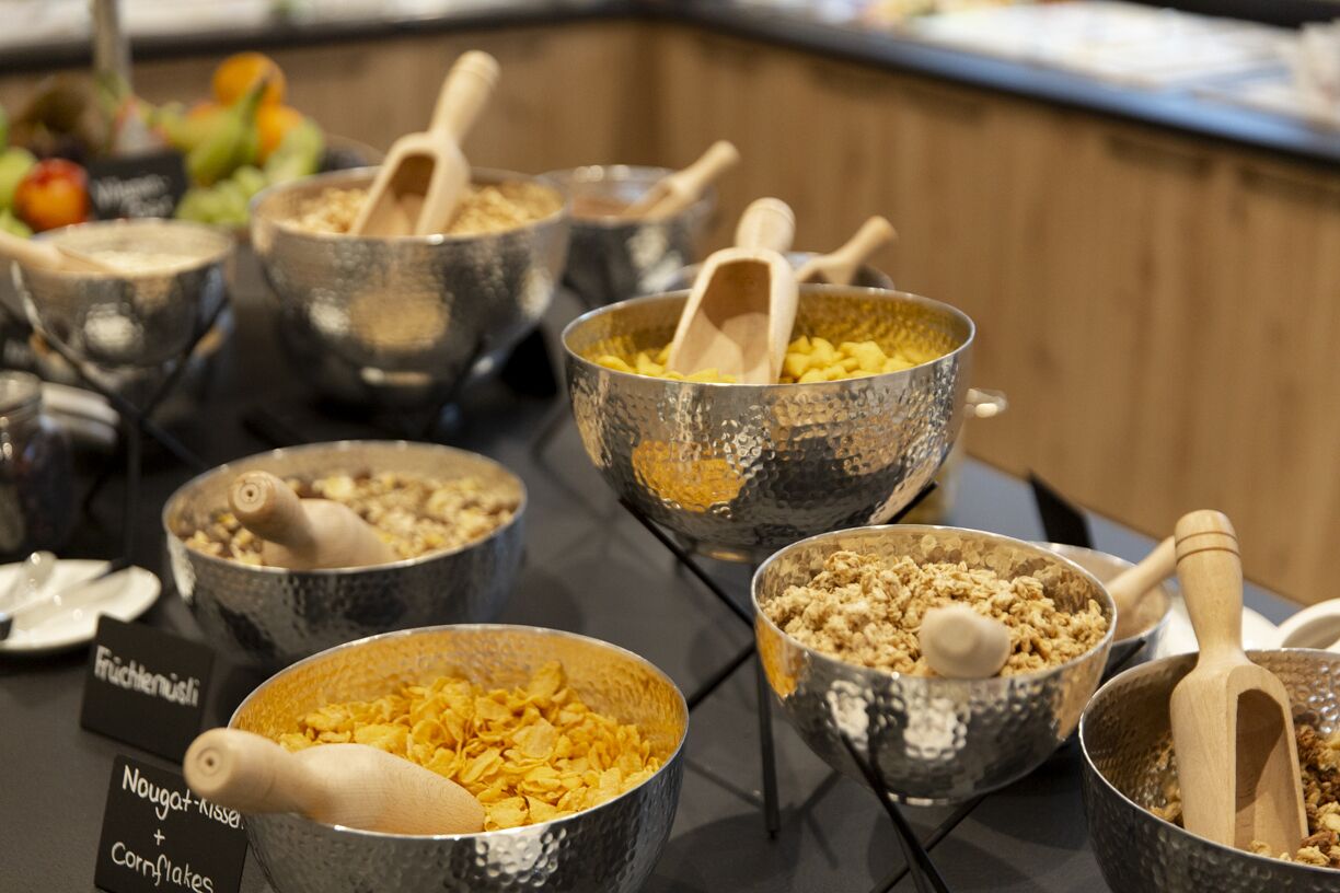A buffet table with various food items in metal bowls, including cornflakes and granola.