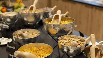 Un tavolo per buffet con diversi cibi esposti in ciotole metalliche, tra cui cornflakes e granola.