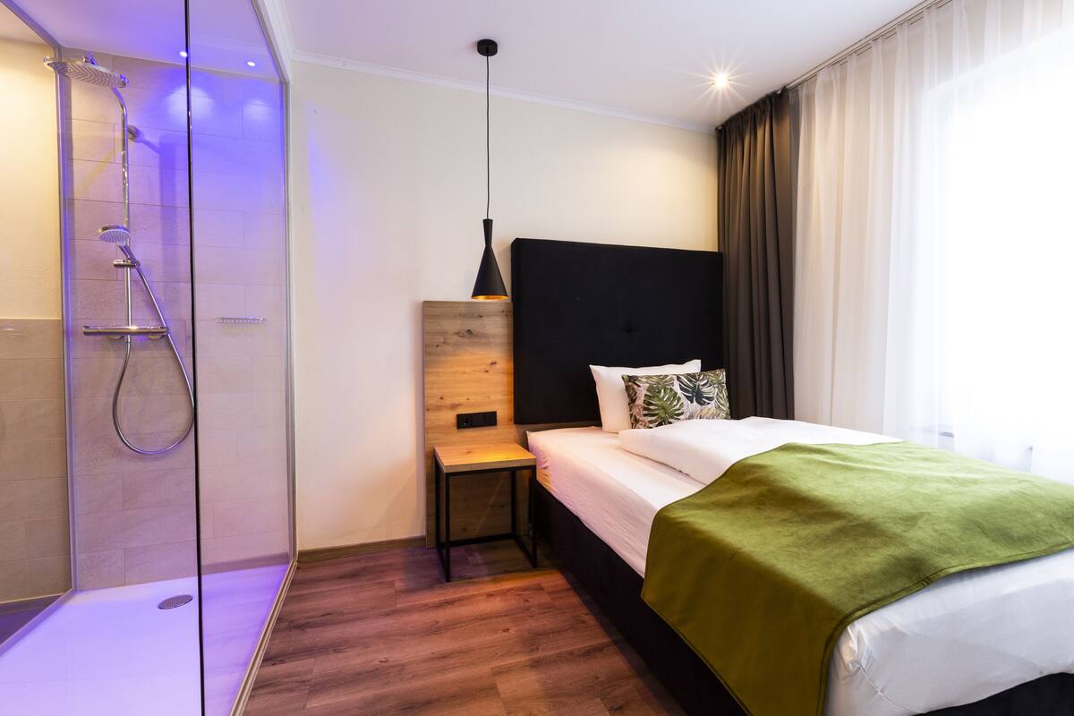 Ein Hotelzimmer mit Dusche, einem Nachttisch, einem Bett mit grüner Decke und einem schwarzen Kopfteil.
