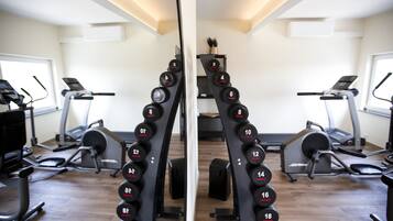 A gym with mirrored walls, exercise equipment, and a wooden floor.