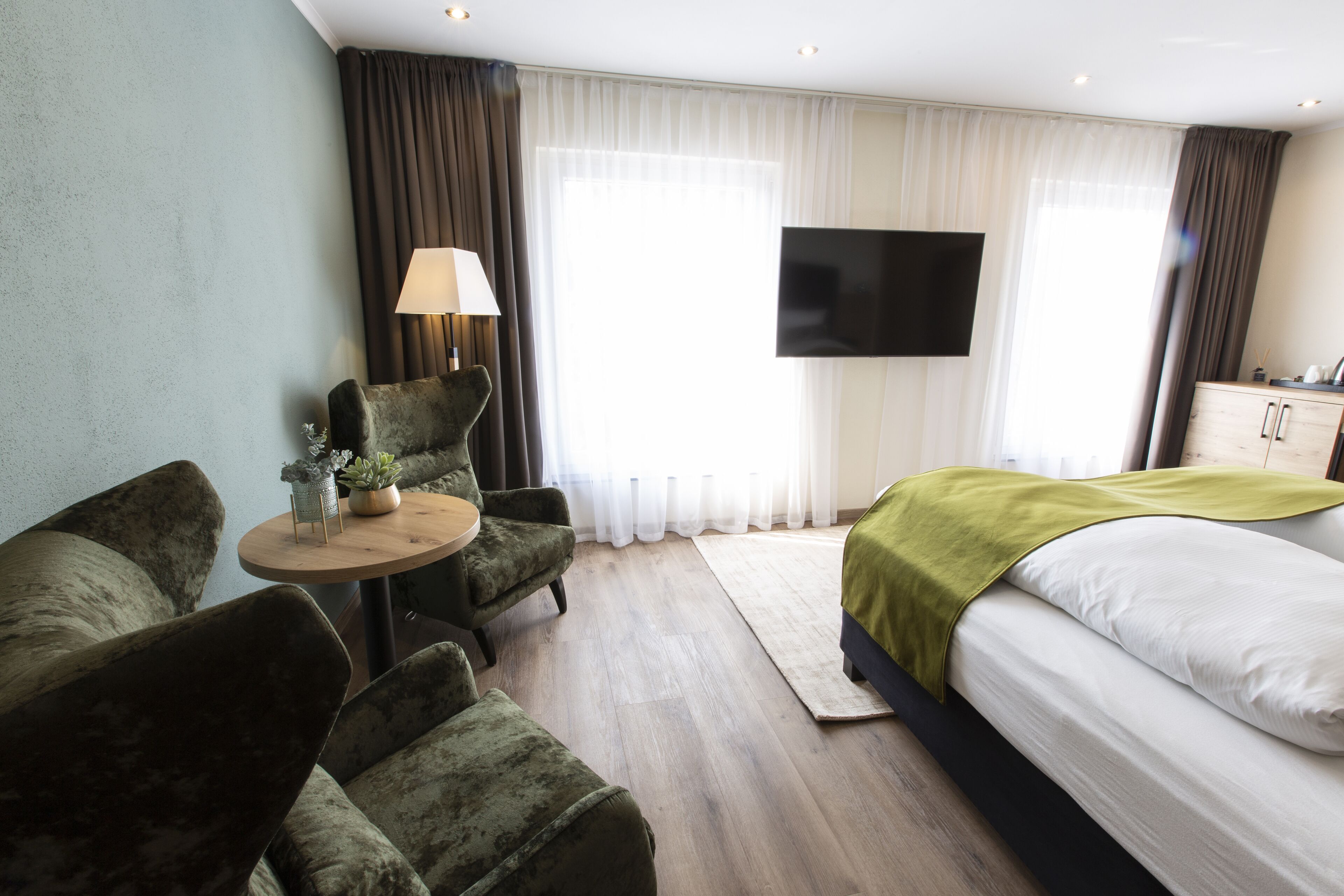 Una habitación de hotel con cama, escritorio, silla, televisión y ventana con cortinas.