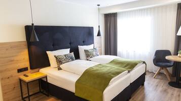 Una habitación de hotel moderna con una cama grande, una mesita de noche, una silla y un ventanal con cortinas.