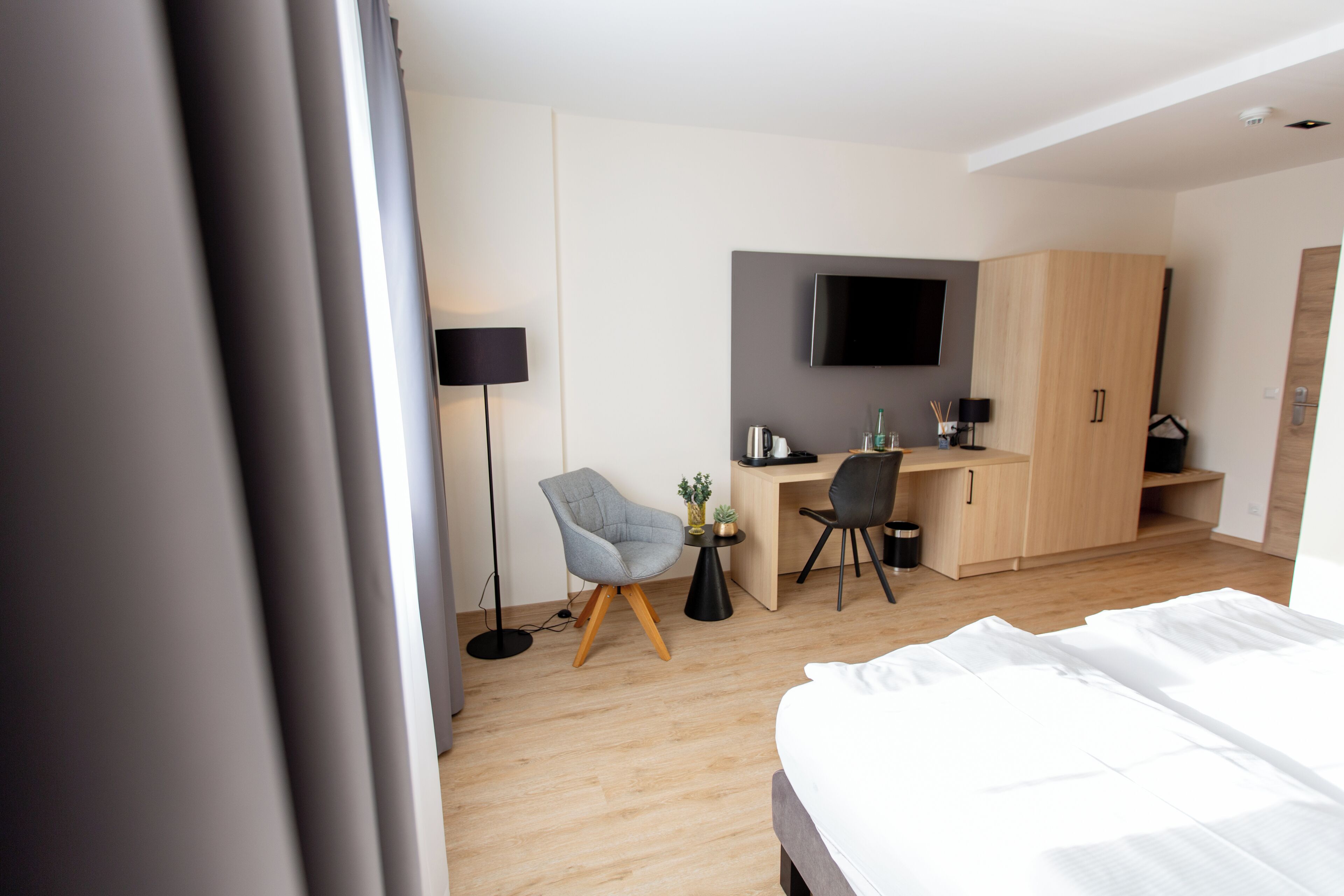 Ein modernes Hotelzimmer mit Bett, Schreibtisch, Stuhl, Fernseher und Kleiderschrank.