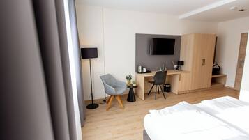 Ein modernes Hotelzimmer mit Bett, Schreibtisch, Stuhl, Fernseher und Kleiderschrank.