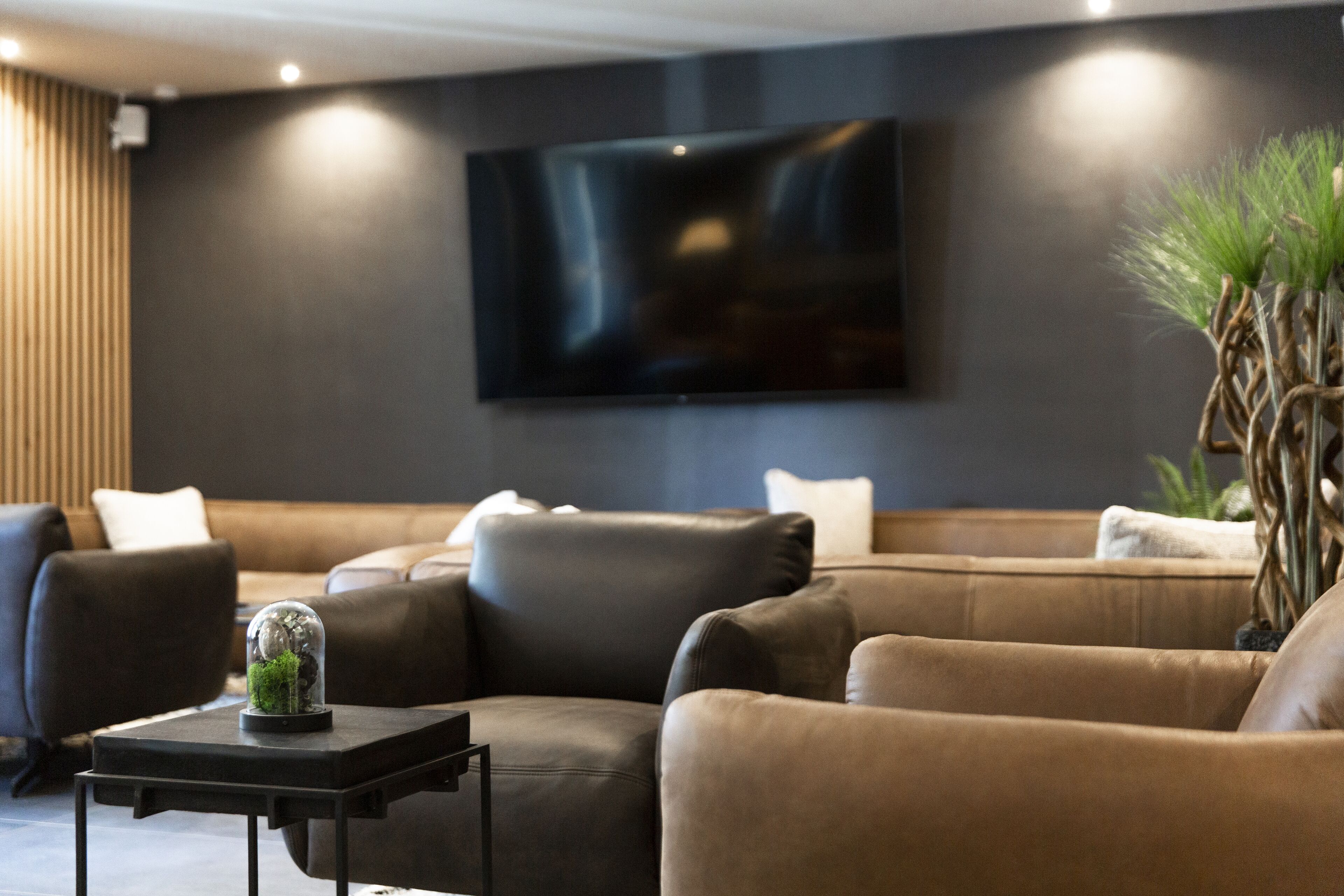 A modern living room with a sectional sofa, a small side table, and a large flat-screen TV mounted on the wall.