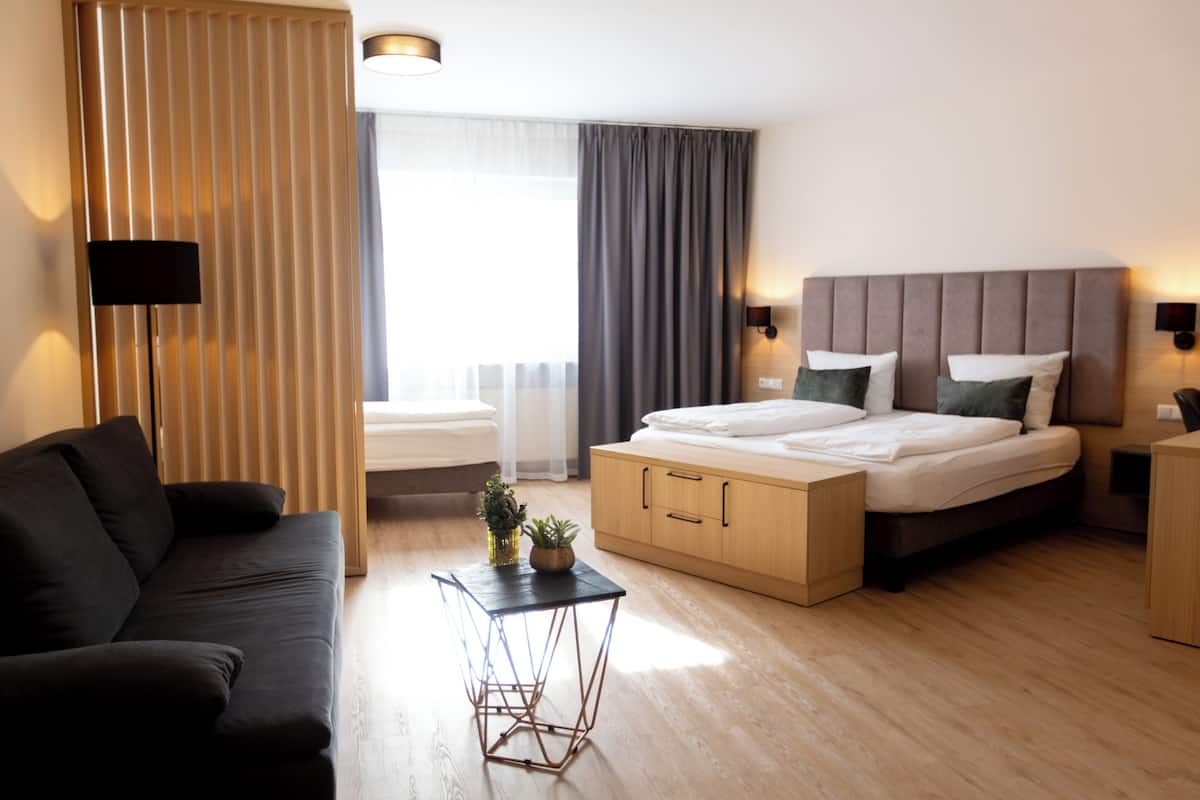 Ein modernes Hotelzimmer mit Bett, einer Couch, einem kleinen Tisch mit Pflanze und einem fenster mit Vorhängen.