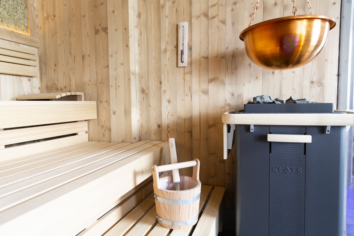 A wooden sauna with benches, a copper basin, and a sauna heater.