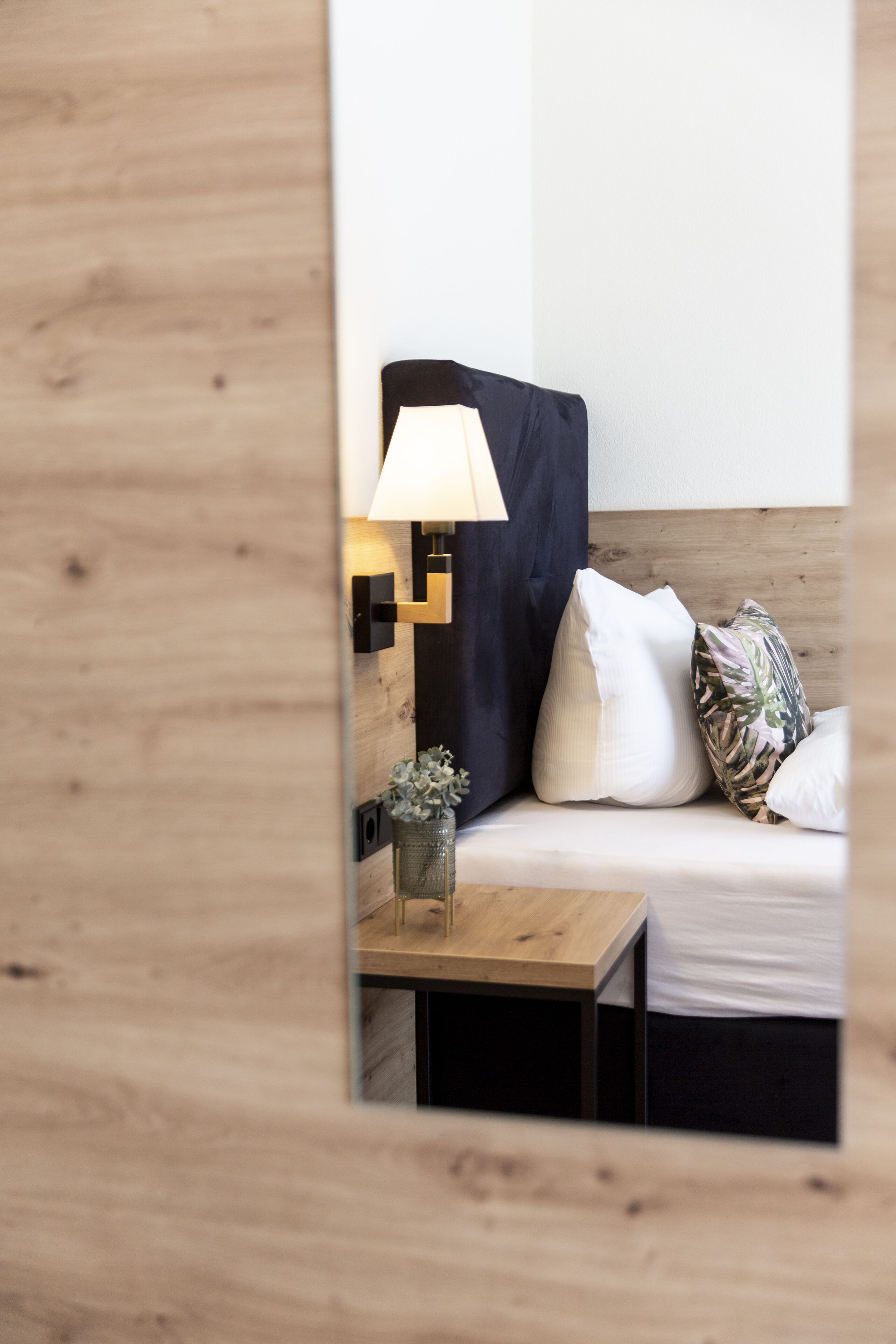 A neatly arranged hotel room with a bed, a bedside table, a lamp, and a small decorative plant.