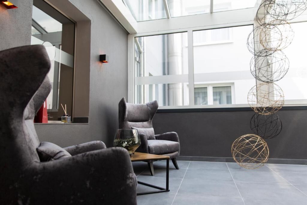 Un interior moderno con sillas tapizadas en gris, una mesa de madera y un ventanal con vistas a la ciudad.