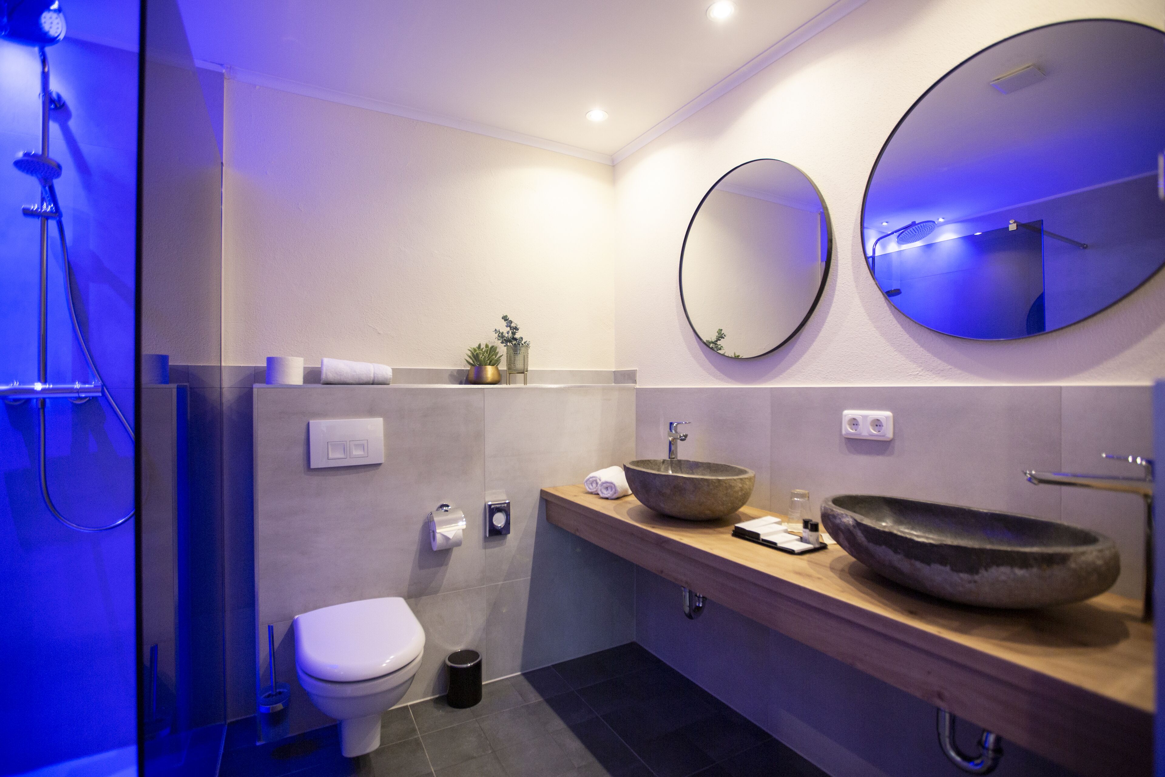 A modern bathroom with a large round mirror, a vessel sink, and a shower area.