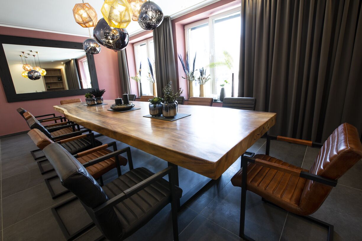 A modern dining area with a wooden table and leather chairs, surrounded by large windows and potted plants.