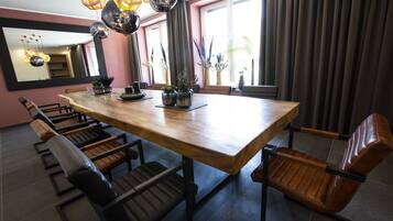 A modern dining area with a wooden table and leather chairs, surrounded by large windows and potted plants.