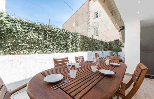 Uma área de refeições ao ar livre com mesa de madeira preparada para quatro pessoas, rodeada por cadeiras.