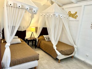 Habitació d'hotel amb dos llits, cadascun amb un llençol damunt i coixins, una taula de nit amb una làmpada i una paret amb un cartell que diu 'Smile'.